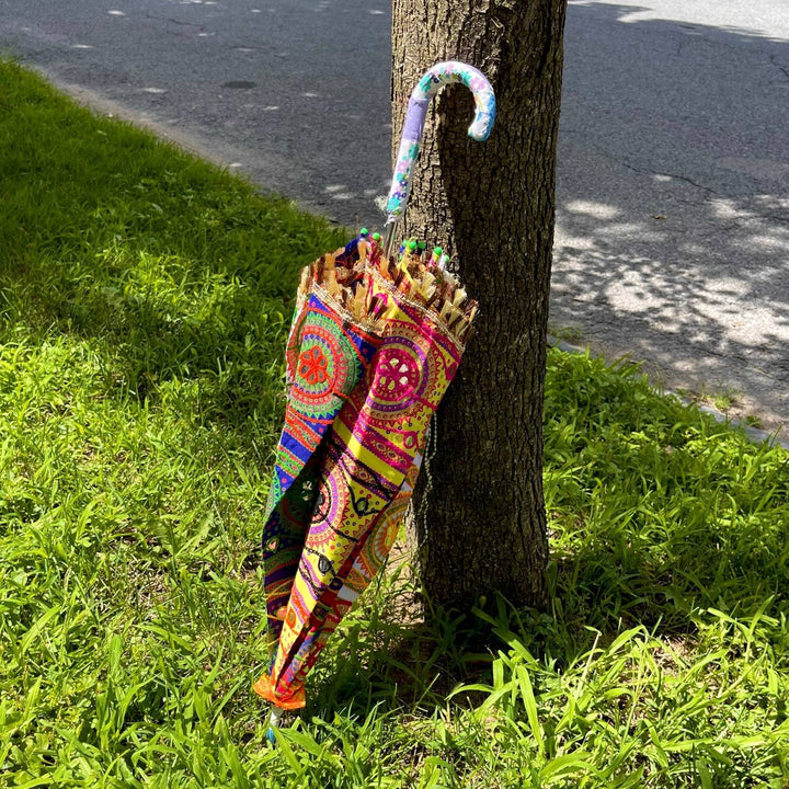 Embellished Parasol Umbrella folded up leaning against a tree,