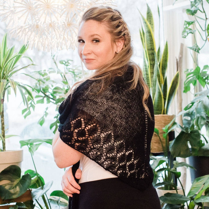 Model wearing lace weight silk shawl in black with potted greenery in the background