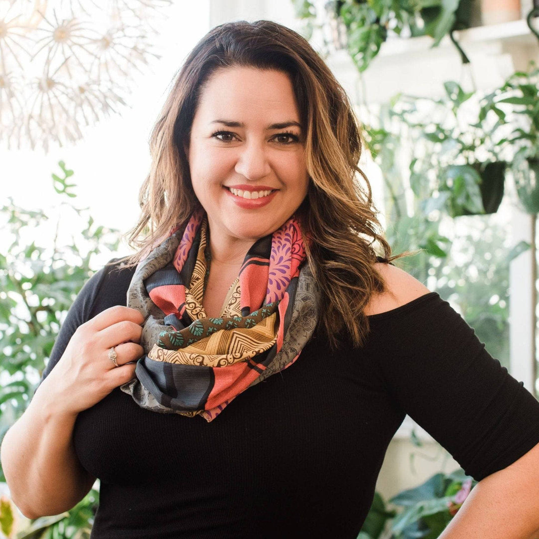 A woman smiling, wearing a colorful patterned scarf, in a plant-filled background.