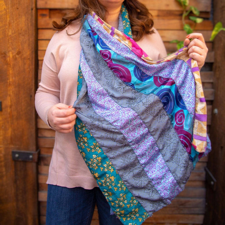 Woman in pink sweater holding colorful patterned scarf. Blue, purple, and gold designs visible.
