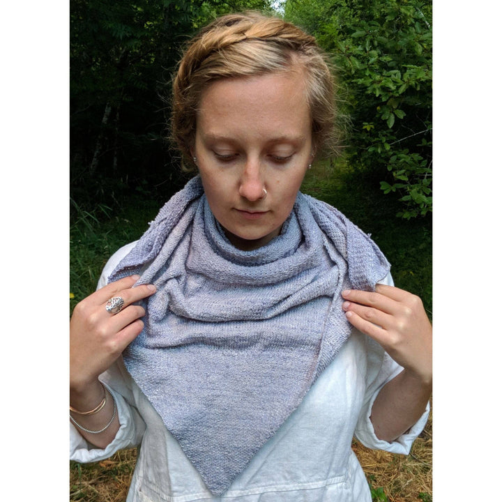 Model wearing serendipity lace weight shawl in grey in front of a wooded background.