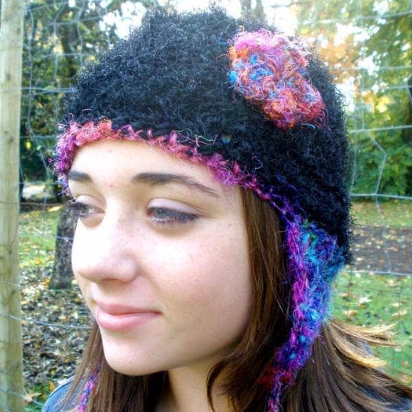 A woman wearing a black hat with multicolored edges and a flower on it, with trees in the background