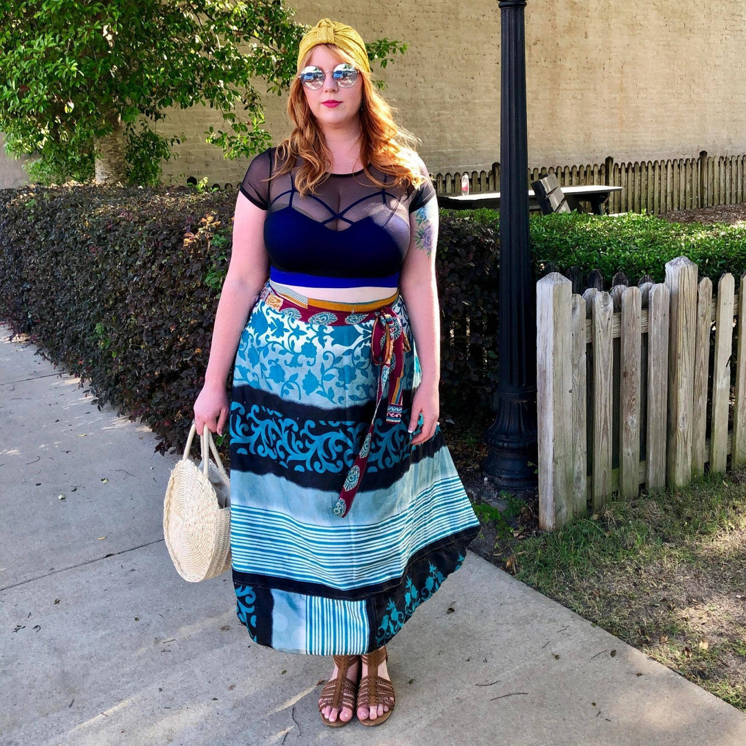 Model is standing on a sidewalk wearing a tea length sari wrap skirt in blue.