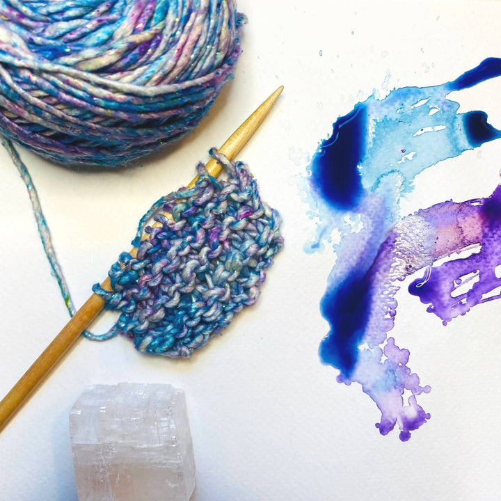 Close-up of knitted swatch, yarn, and watercolor art.