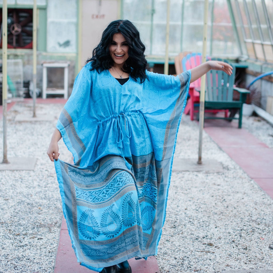 Model is dancing wearing a light blue aanya long kaftan while standing in a greenhouse. 