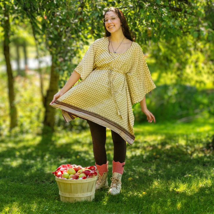 Woman standing next to a basket of apples in a forest wearing a pale yellow shorty kaftan