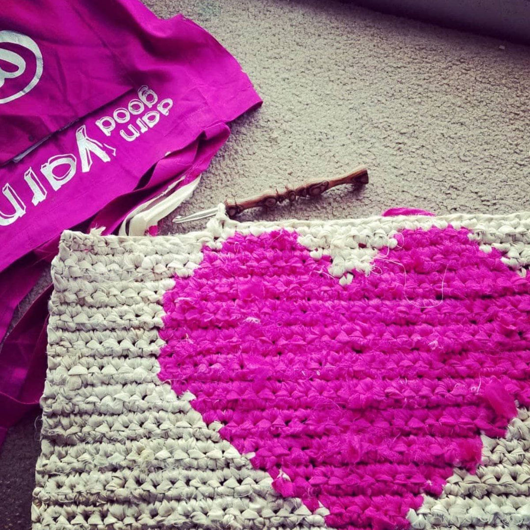 All My Love crochet Wall Hanging with hot pink heart sitting on beige carpet next to a hot pink Darn Good Yarn tote bag