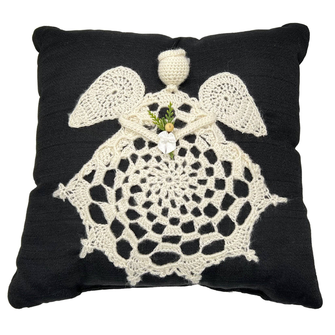 Ecru crochet Angel applique stitched onto a black pillow in front of a white background.