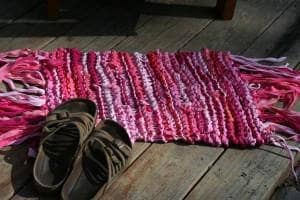 knit Area Rug Pattern in pink colors on a wooden surface with brown sandals