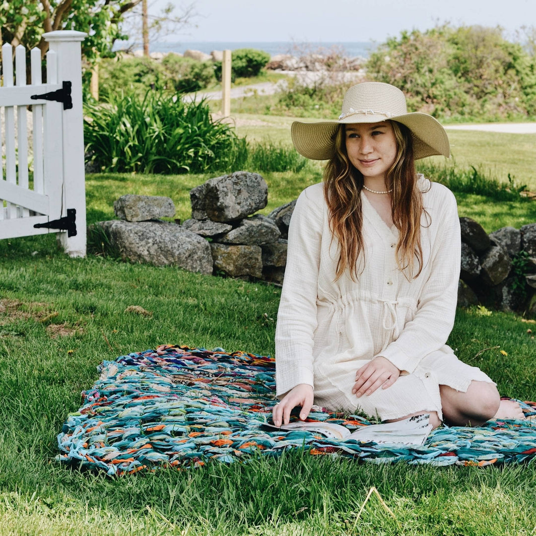 Model sitting on an arm knit recycled chiffon blanket in the grass with greenery in the background.