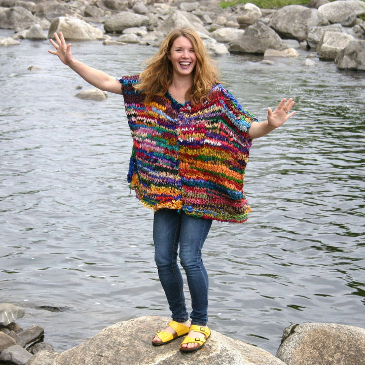 Founder Nicole Snow wearing artfully yours poncho while standing on a boulder with lake in the background.