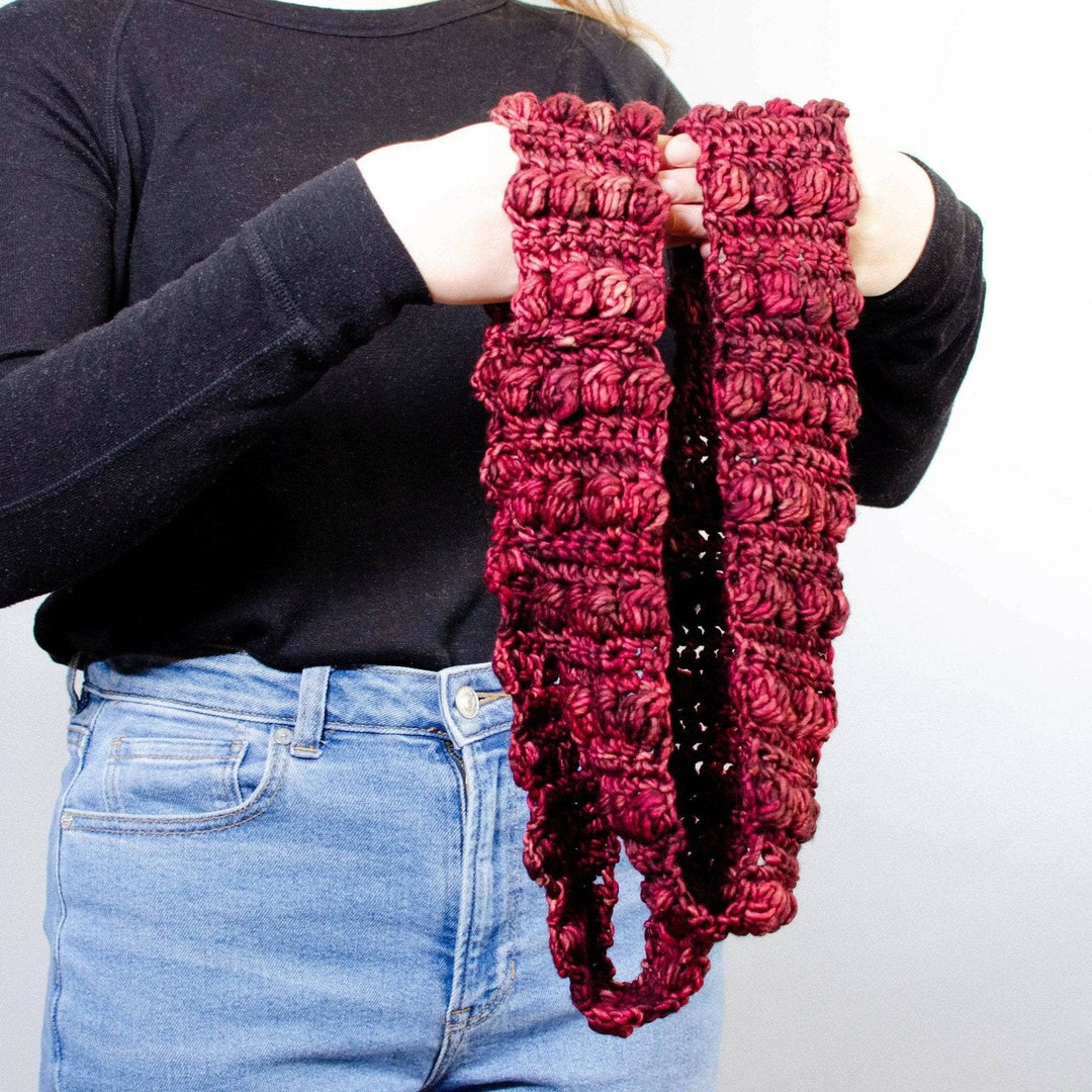 Person wearing a black shirt and jeans hold a red infinity scarf