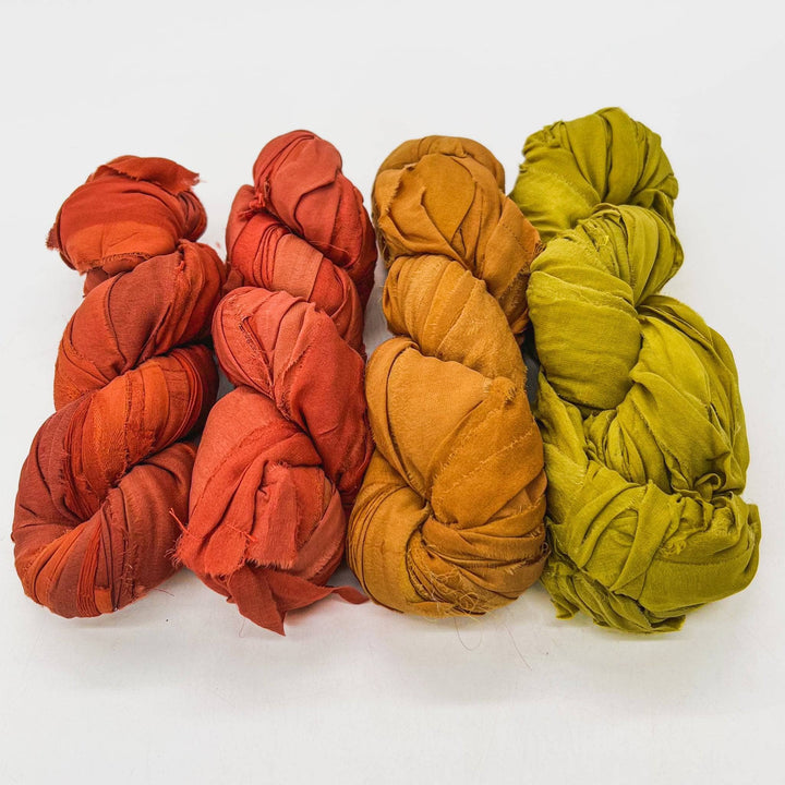 Bonfire chiffon ribbon yarn ombre pack in front of a white background. Left to right: Orange spice, bright orange, golden yellow, chartreuse..