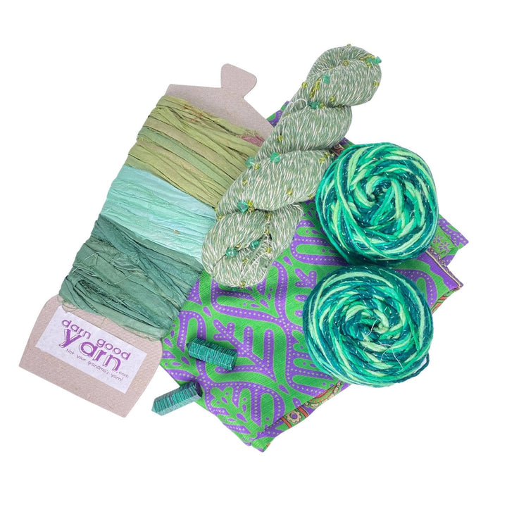 Malachite energy bundle with all items showing in front of a white background. 2 malachite crystals, 2 skeins sparkle worsted weight silk, 1 skeins chakra beaded cotton yarn, 3 color sari silk ribbon sample card, and coordinating furoshiki.
