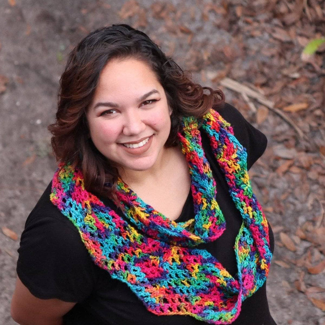 Woman wearing black tee shirt and multicolored crochet scarf and standing in the woods