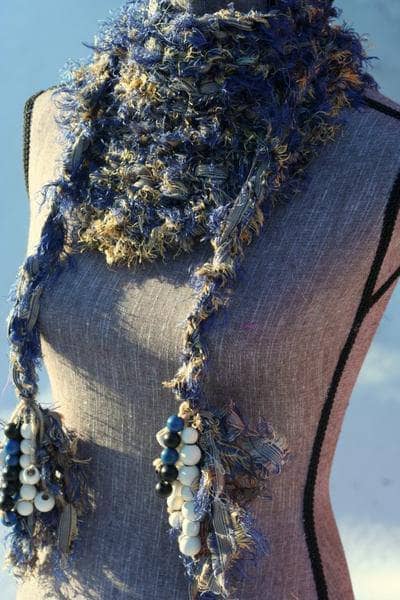 Mannequin wearing a neutral colored fuzzy knit scarf with a blue sky background