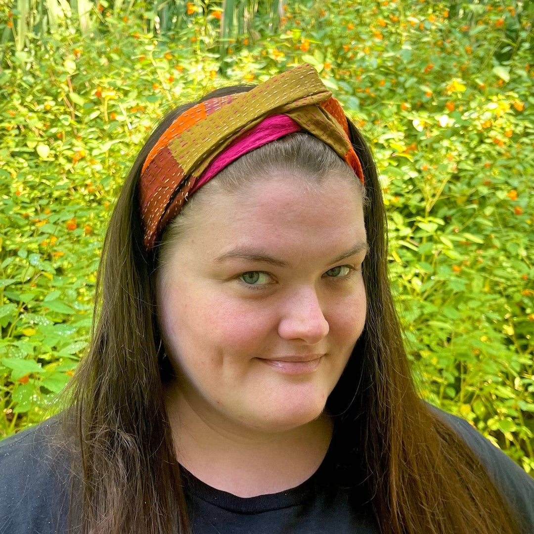 A woman standing outside wearing a black tee and a fall colored kantha headband in her hair.