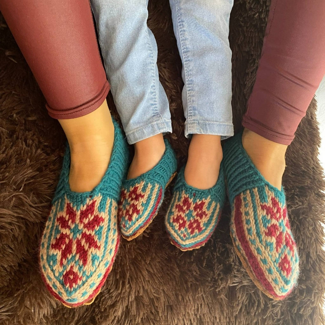 Close up of adult model and child model wearing folklore slippers. Background is a brown shaggy rug. 