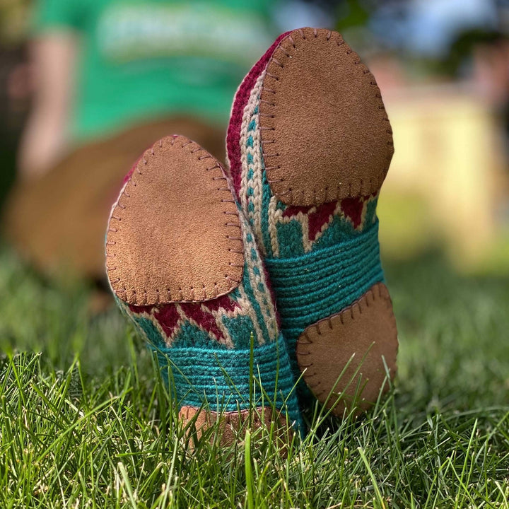 Model wearing handmade blue, burgundy and cream slippers with a tan soles laying on the grass
