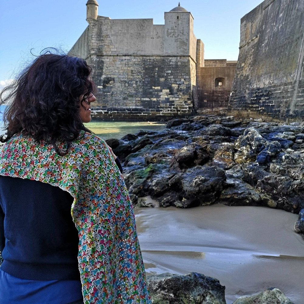 Person wearing a grey and rainbow wrap on a beach with a castle in the background