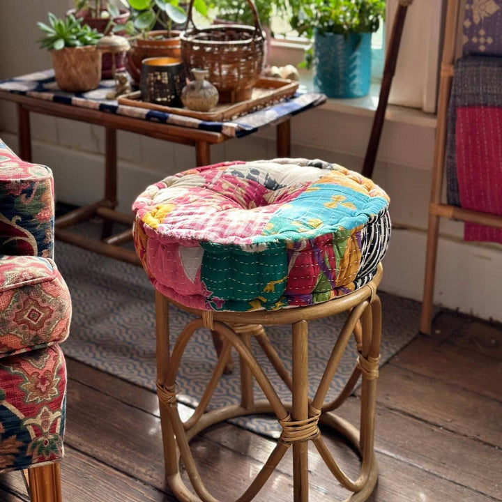 A patchwork pouf pillow on top of a bamboo ottoman. 