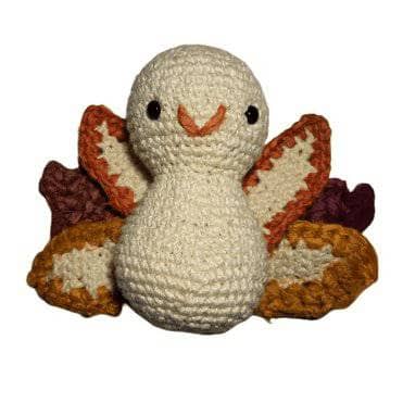 White amigurumi turkey with yellow, orange and brown feather tips on a white background