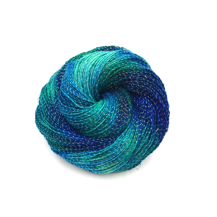 Lace weight silk yarn in color sparkle enchanted forest (blue, green and sparkle) in front of white background.