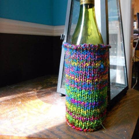 green bottle covered in a yarn sleeve on a floor and a lamp behind it