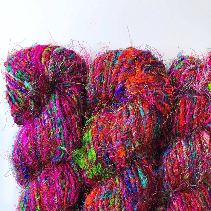 Close up of three skeins of Darn Good Yarn hand-spun sari silk yarn. Colors are vibrant and mixed, many reds blues, pinks and purples throughout.
