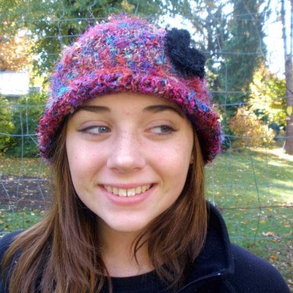 Girl smiling wearing a multicolor beanie with a black flower on it