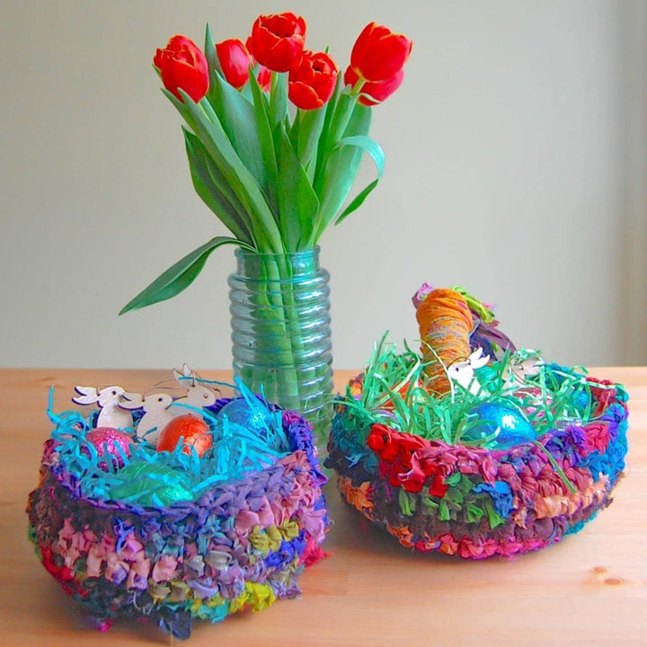 two colorful baskets of ribbon yarn with confetti inside and a flower pot with a flower in between on top of a table