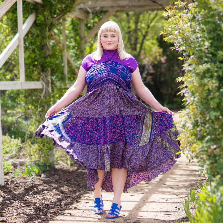 Girl stands in front of a flowery landscape and wears a purple sedona dress