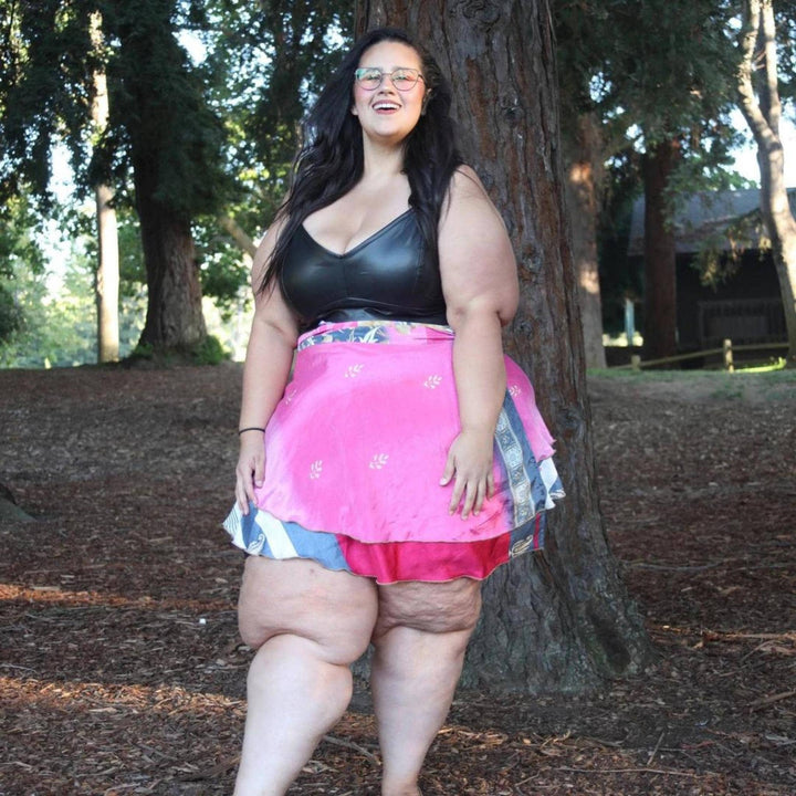 Goddess Model standing in a wooded area wearing a pink sari wrap mini skirt. 