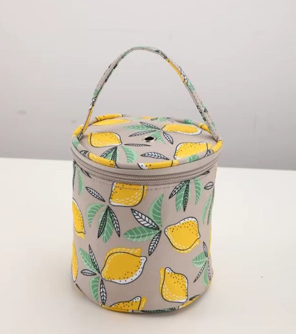 A cylindrical insulated lunch bag with a handle, featuring a pattern of yellow lemons and green leaves on a light gray background.