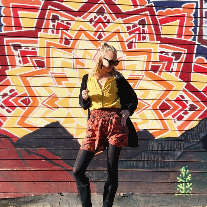 Woman in colorful outfit posing against a mandala mural.