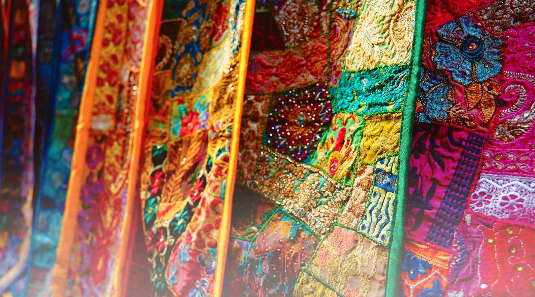 Close-up of multicolored sari fabrics made with reclaimed stitched-together sari material. Slight "to-white" gradient applied to bottom of image.