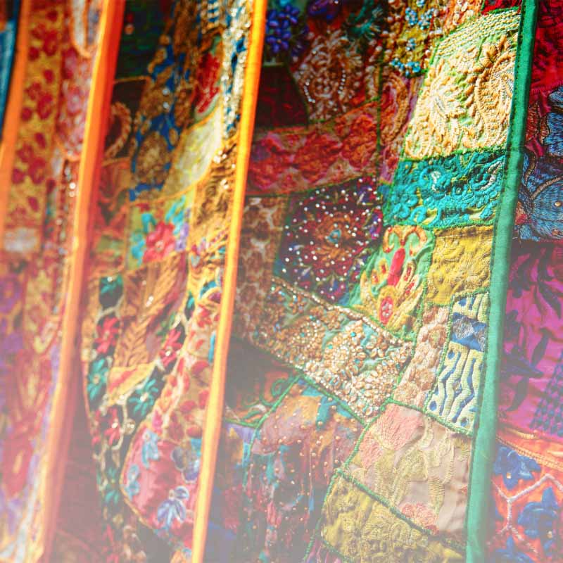 Close-up of multicolored sari fabrics made with reclaimed stitched-together sari material. Slight "to-white" gradient applied to bottom of image.
