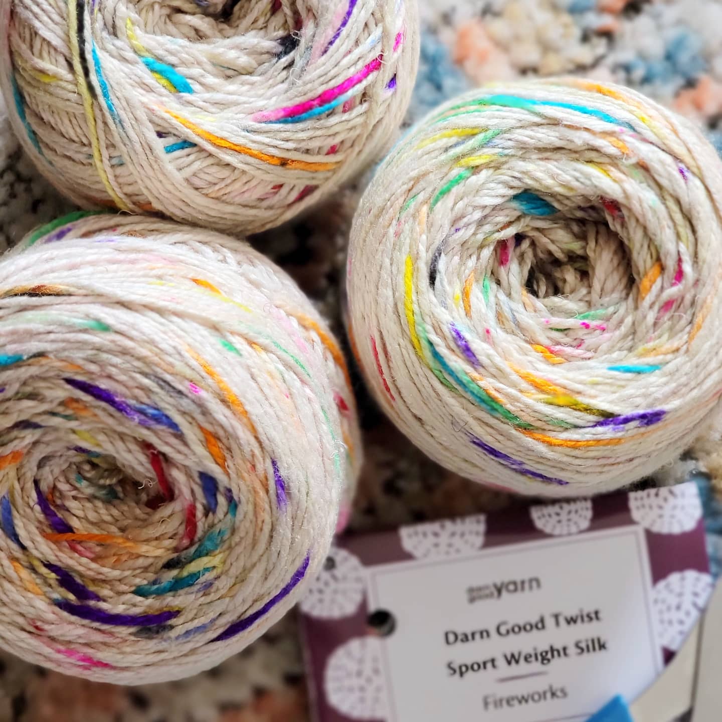 Sport weight silk yarn in fireworks variant stacked together with Darn Good Yarn tags