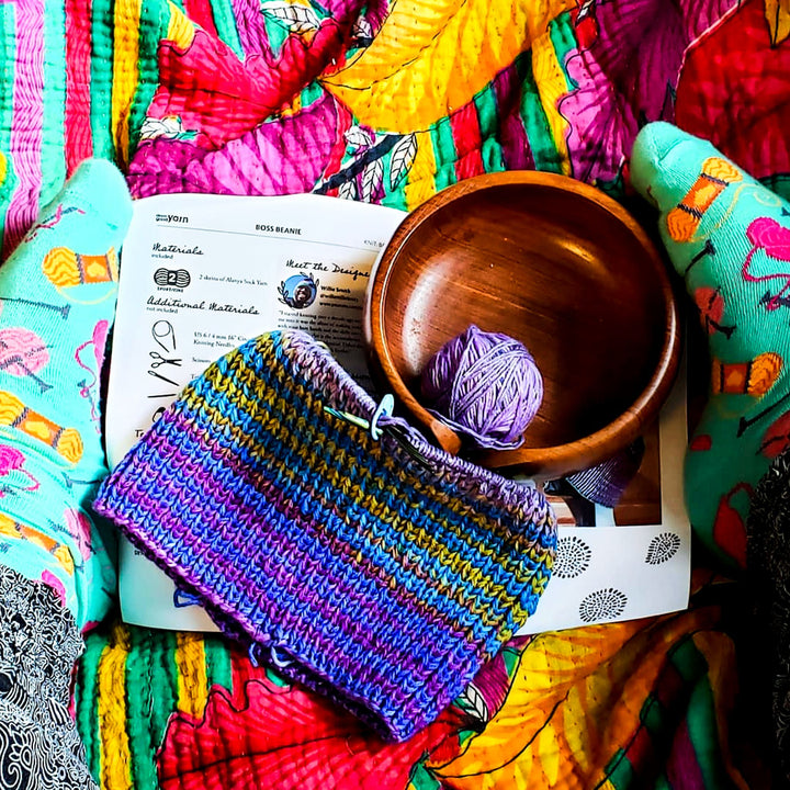 Knitted fabric with yarn and a wooden bowl laid out on a vibrant cloth.