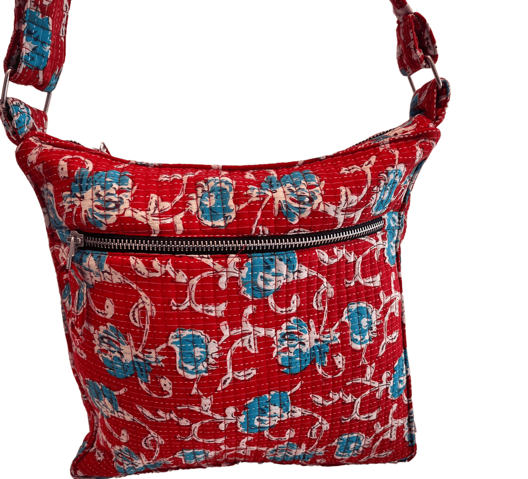 A red quilted bag with a floral pattern in blue and white. It has a front zipper pocket and an adjustable strap.