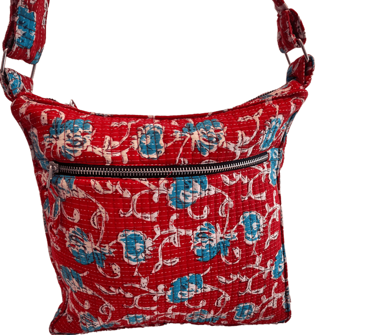 A red quilted bag with a floral pattern in blue and white. It has a front zipper pocket and an adjustable strap.