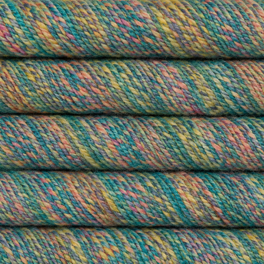 Close-up of folded yarn or thread with a variegated multicolor pattern of teal, green, yellow, pink, and orange.
