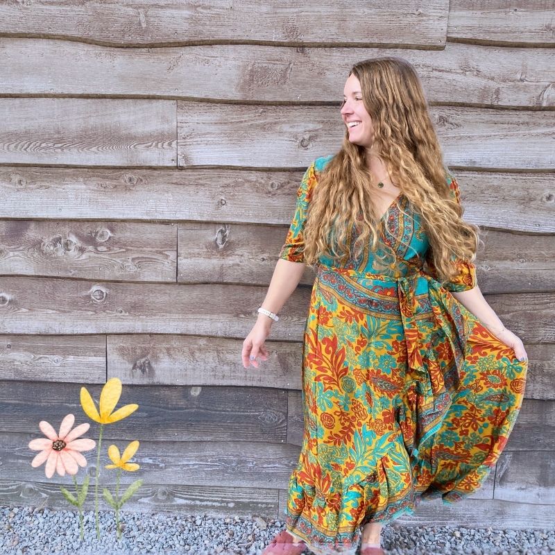 Woman in a colorful floral dress standing against a wooden wall with flowers added to the scene.