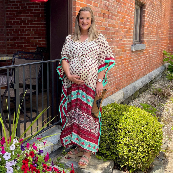 Smiling woman in a patterned kaftan posing near a brick building.