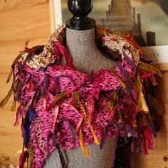 About to Bloom fringe-y pink scarf on a tan mannequin in front of a wooden wall