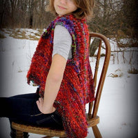 Woman wearing Adventure Cardi vest in multicolor sitting on a wooden chair in front of a snowy landscape