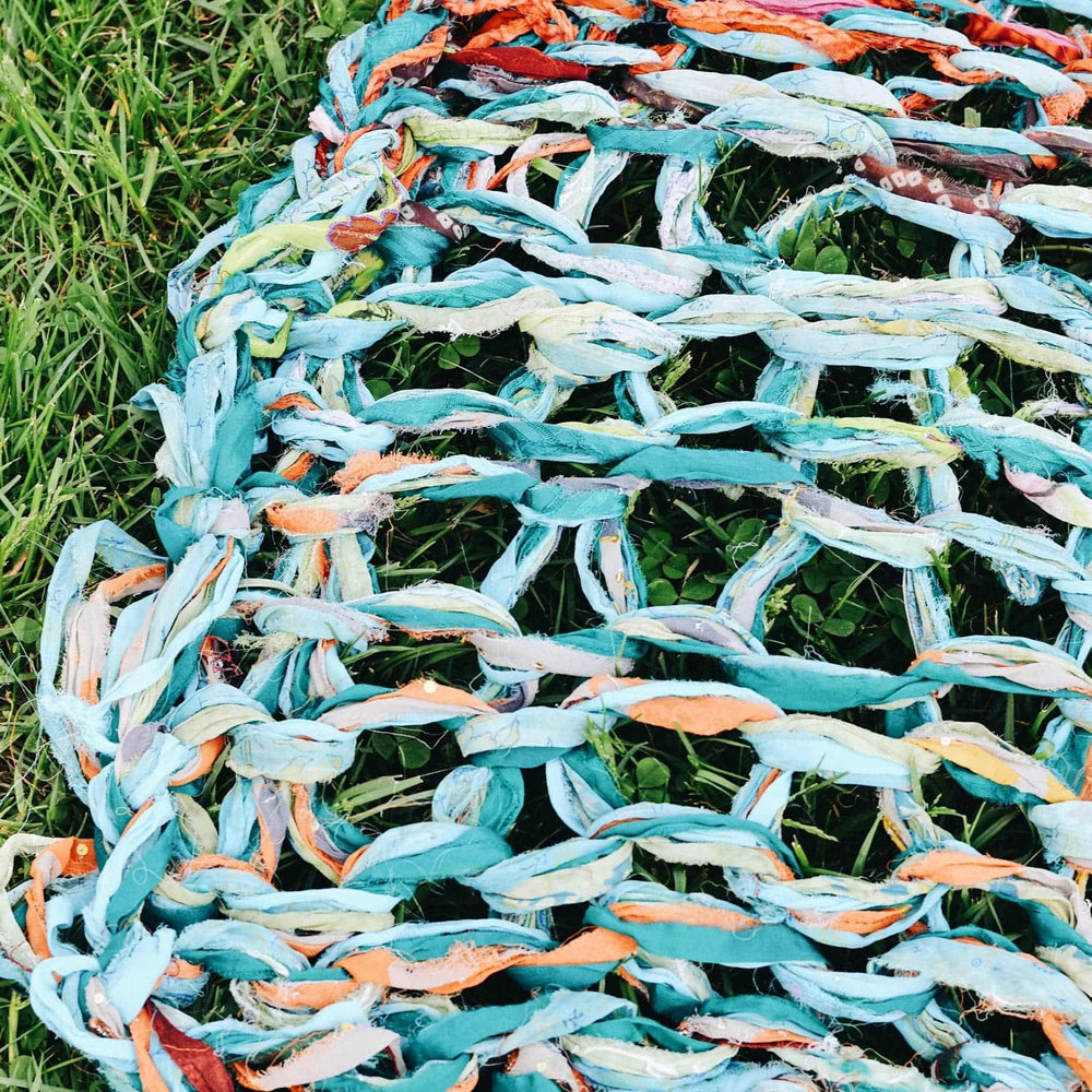 closeup image of arm knit blanket on the grass to show stitch detail.