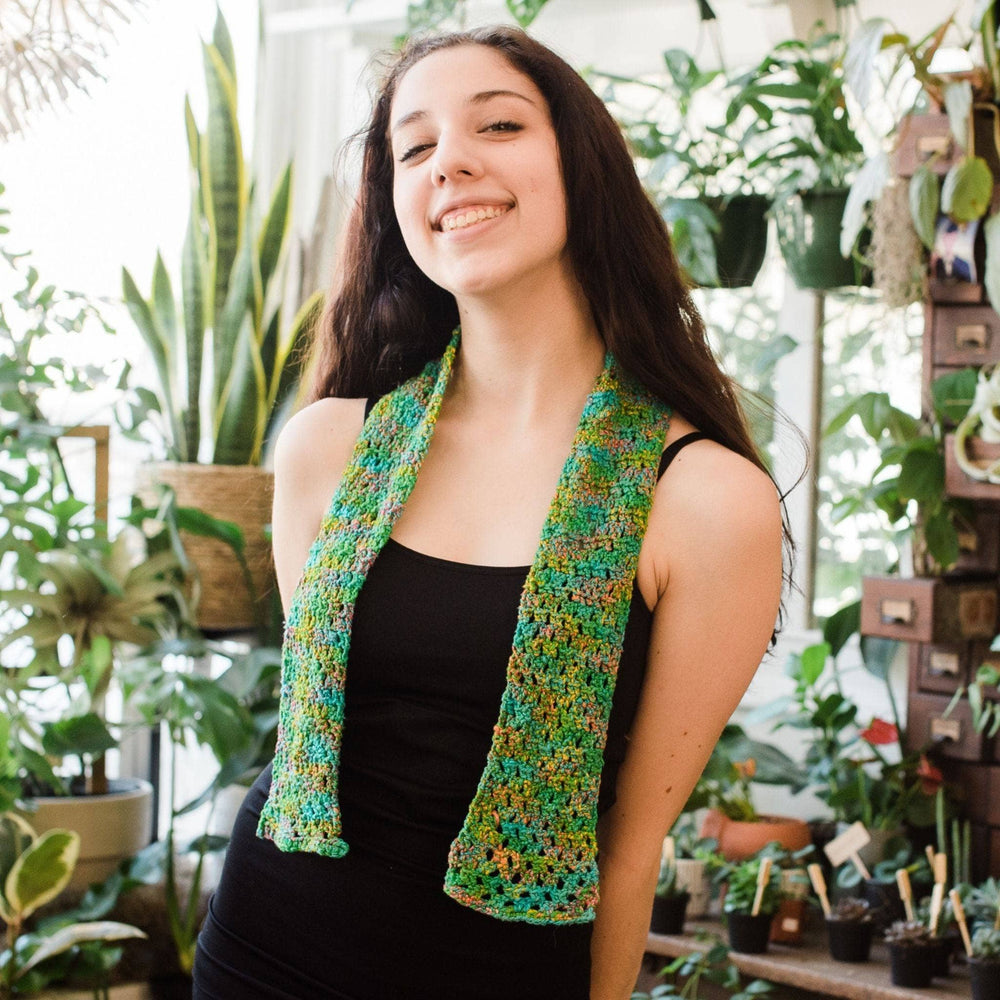 A woman smiling wearing black sleeveless with green scarf.