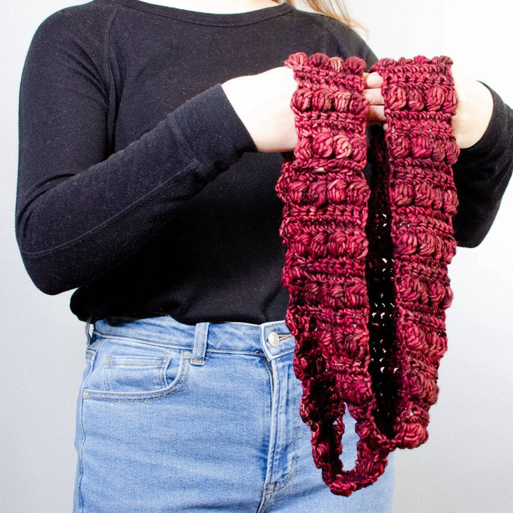 Model is holding a Burst My Bobble Infinity Scarf in front of a white background. 