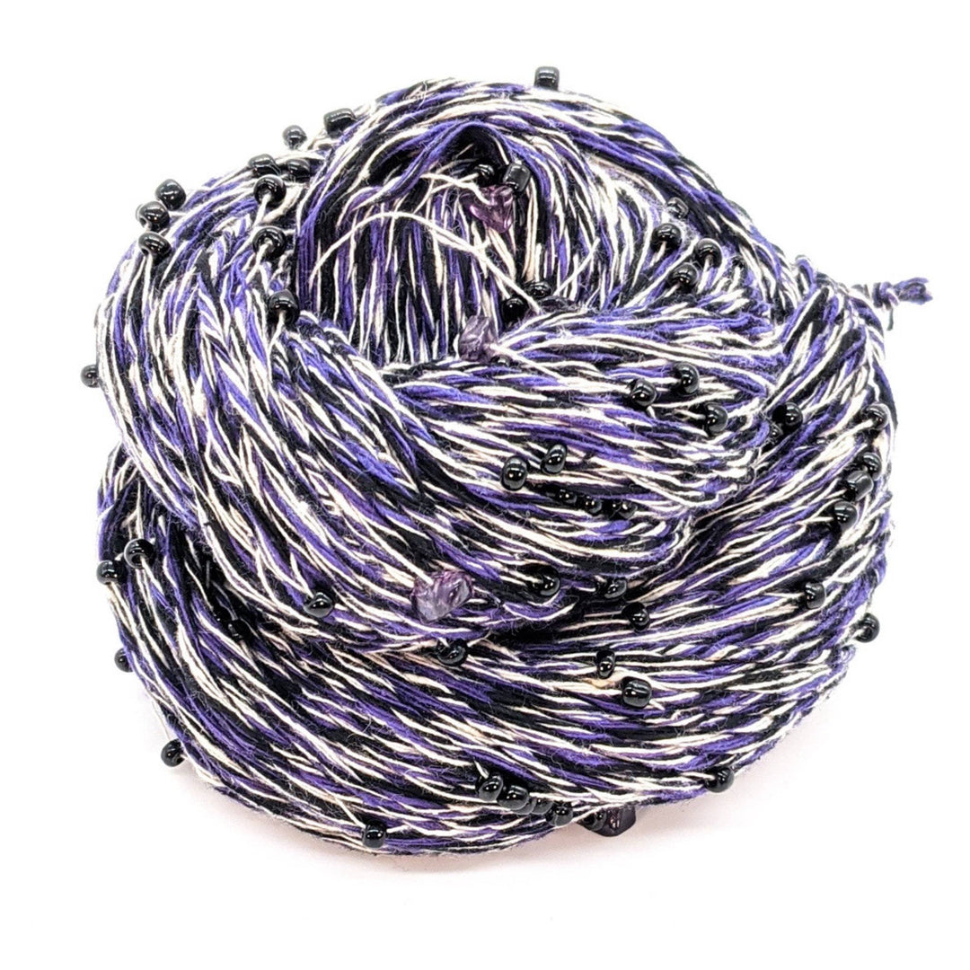 Skein of multicolored yarn in purple, white, and black with small black beads.